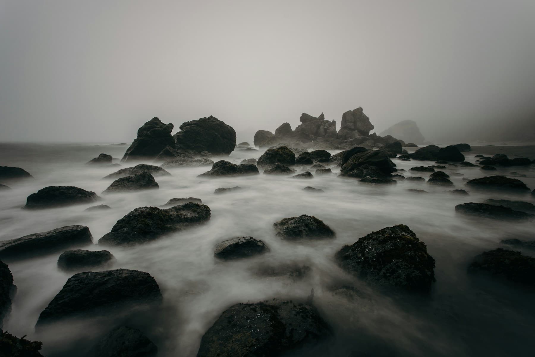 A rocky coastline surrounded by mist and long-exposure ocean waves